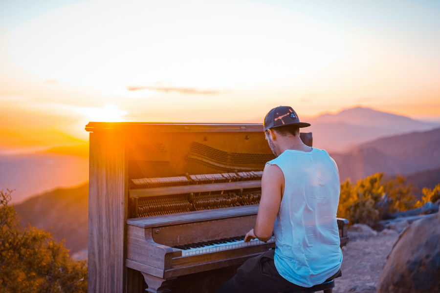 Un hombre tocando el piano al aire libre, en una montaña, durante la puesta de sol.
